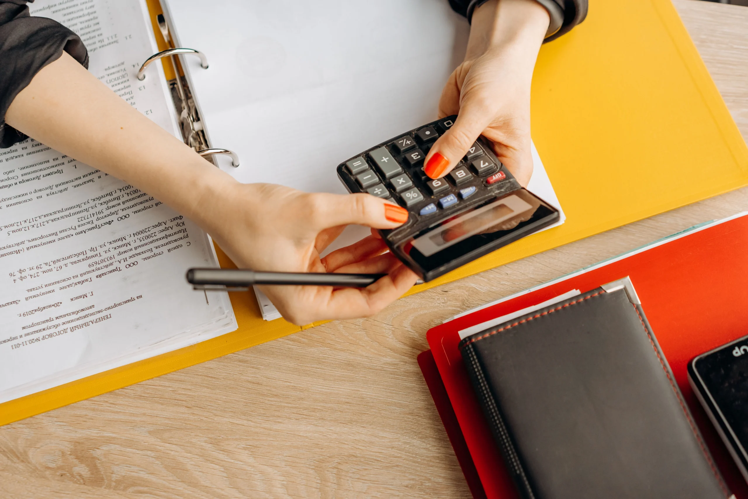 Oil and gas accounting depicted by a woman running numbers on a calculator over a yellow notebook.